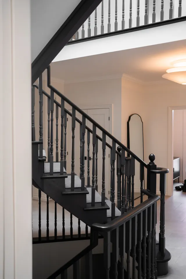 Black-painted staircase with turned balusters rising to a white-railed landing, an arched mirror in the hall beyond