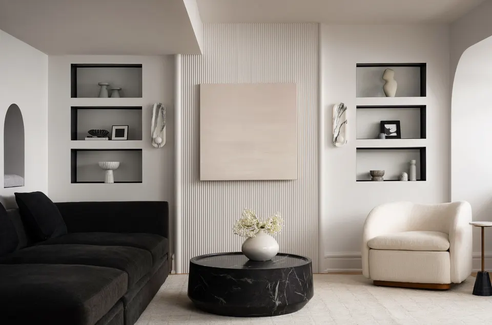 Finished lower-level lounge with a fluted feature wall, lit display niches, a black marble coffee table and a cream bouclé armchair