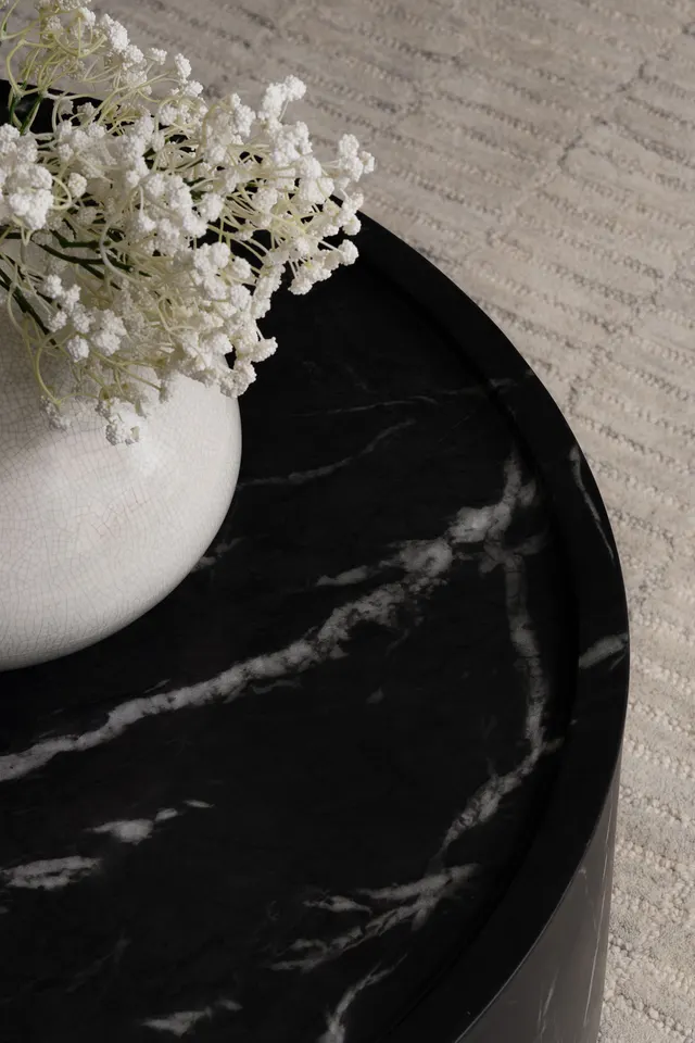 Close-up of the round black marble coffee table, white-veined, beside a vase of baby’s breath