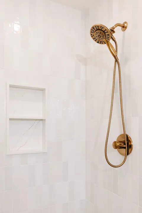 Antique-brass hand shower on white tile beside two recessed niches