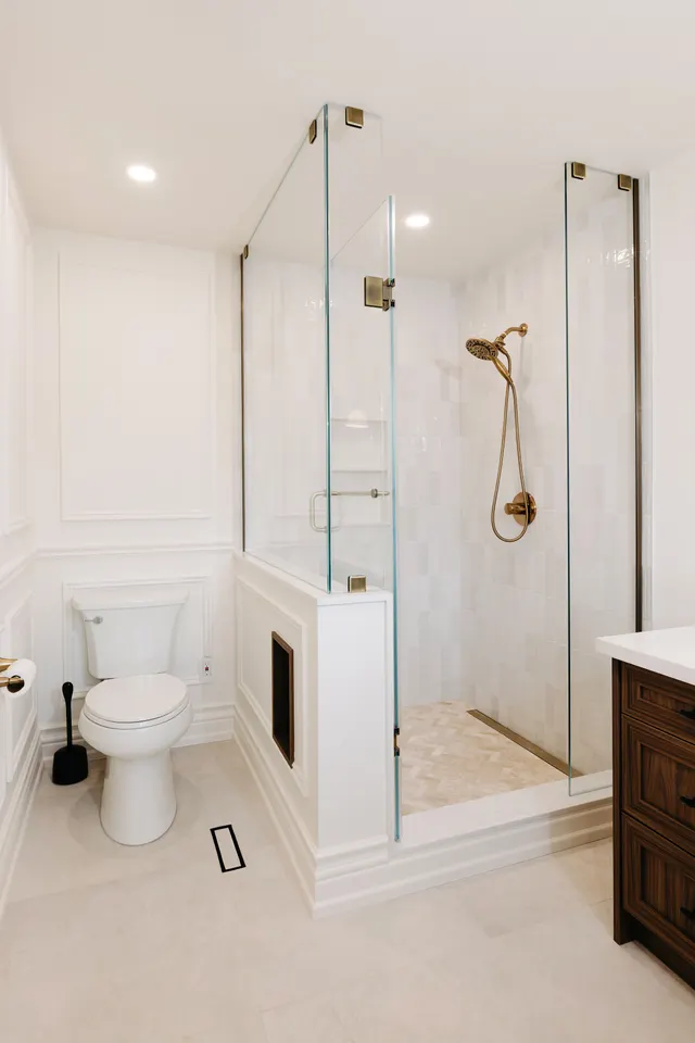 Glass-enclosed shower with white tile, a herringbone marble floor, antique-brass fittings and a recessed niche in the half wall
