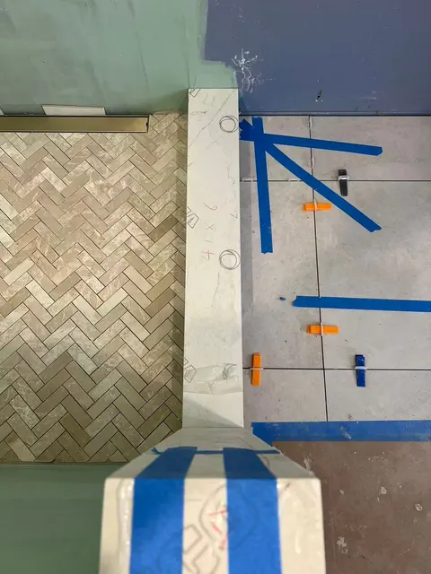 Looking down at the shower floor mid-install: herringbone mosaic, blue tape and levelling clips