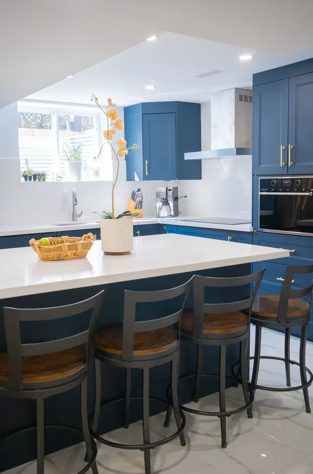 Basement kitchen with blue cabinets and a white quartz island with bar stools