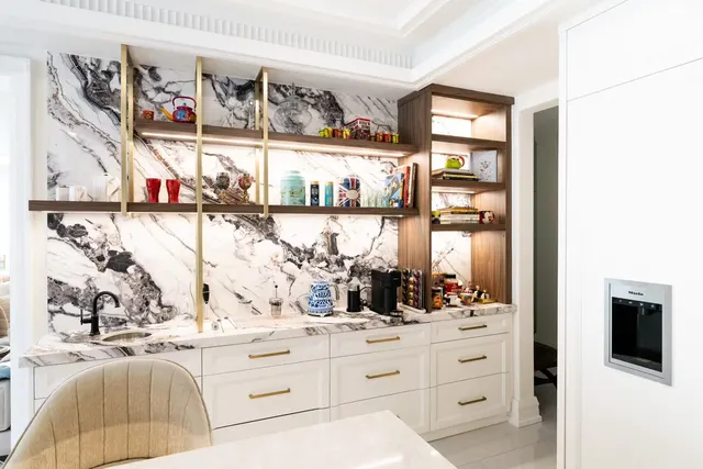 Bold-veined marble slab wall with brass-framed open shelves over white cabinets