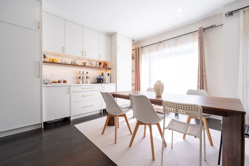Warm white pantry cabinetry with lit open display shelves in the middle, beside the dining table