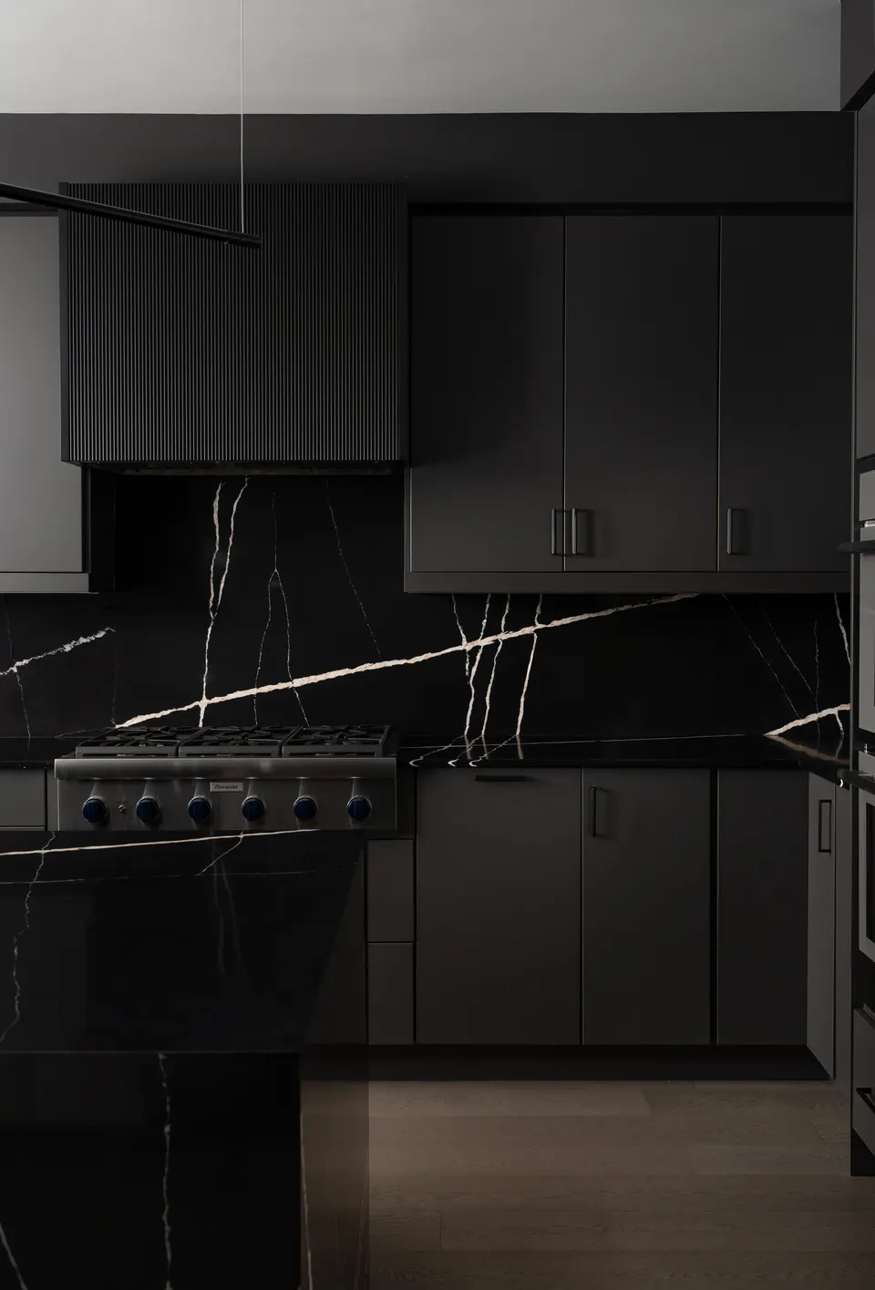 A black marble backsplash behind a stainless range top, under charcoal fluted and slab cabinets