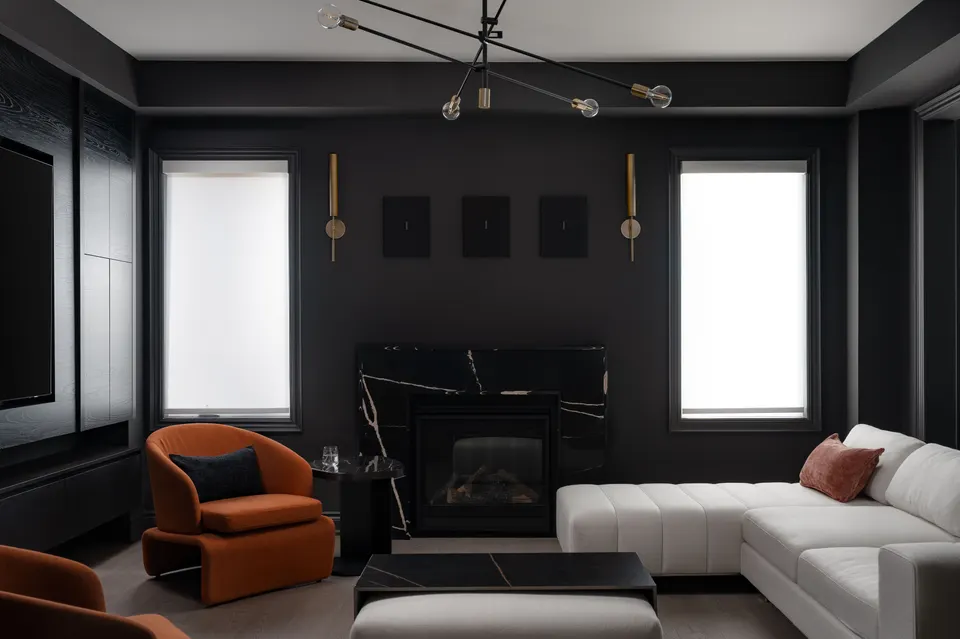 Charcoal-panelled living room with a black marble fireplace, rust-orange lounge chairs and a white sectional