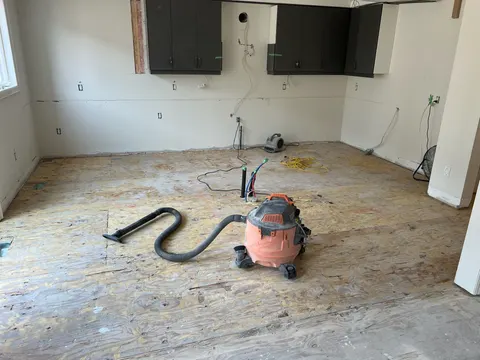 The same kitchen mid-job: stripped to the subfloor beneath the window and upper-cabinet wall