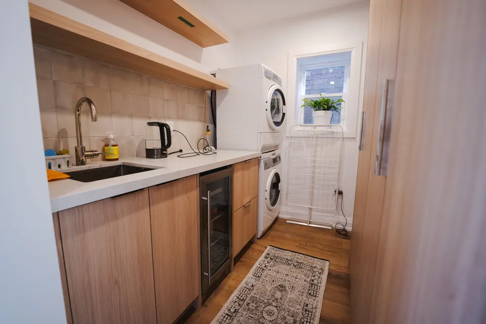 Oak kitchenette with open shelves, a gooseneck faucet, a glass-door fridge, stacked laundry and a small window