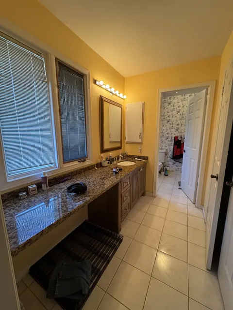 The ensuite before: yellow walls, a long granite vanity and beige floor tile