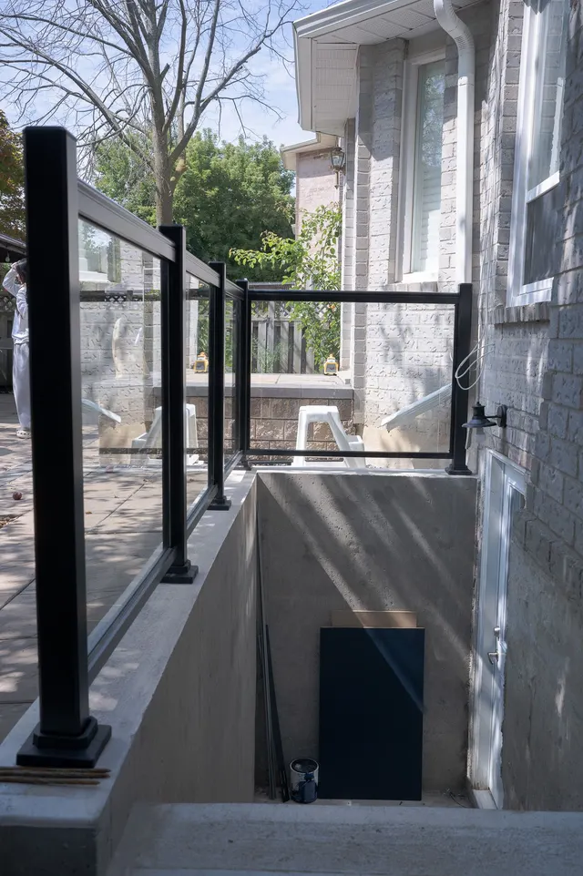 A basement suite’s private walk-up entrance: concrete stairs down to the door behind a black-framed glass guard