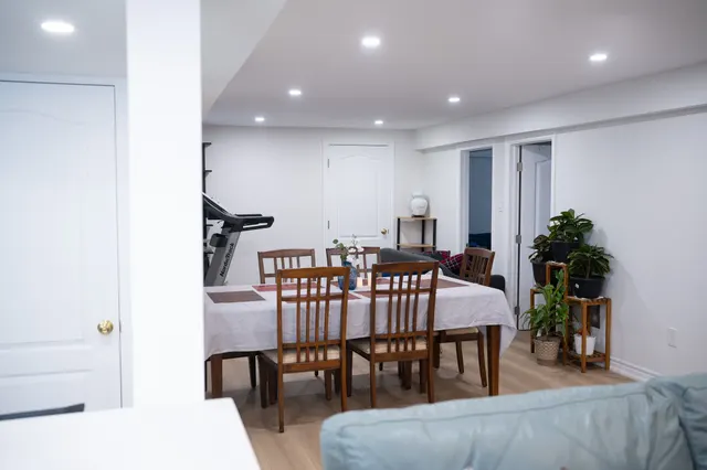 Basement living and dining area with a table for six, a sofa and a treadmill under pot lights