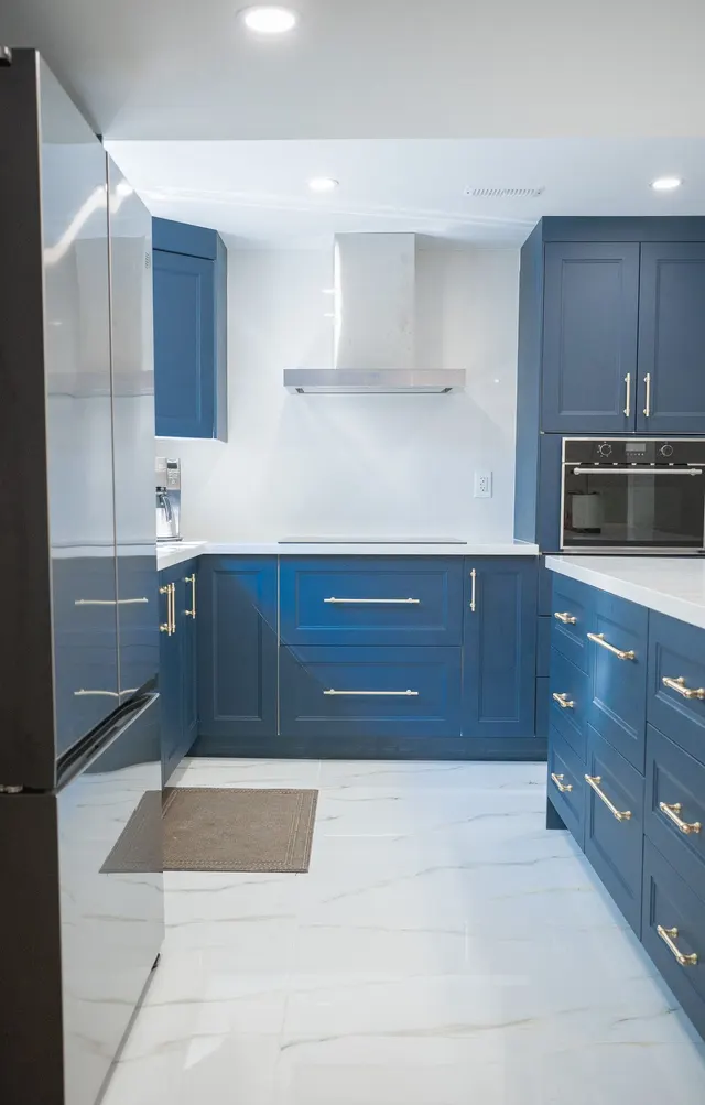 Galley kitchen in a basement suite with navy shaker cabinets, a stainless range hood and white tile
