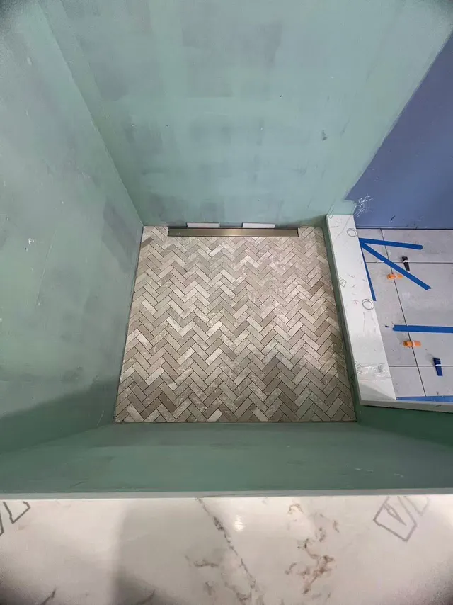Mid-build: shower walls sealed in waterproofing membrane above a herringbone tile base