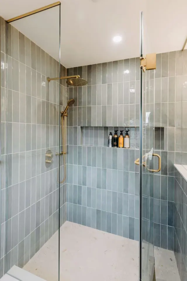 Walk-in shower behind frameless glass, with sage-green tile, a recessed niche and brushed-brass fixtures