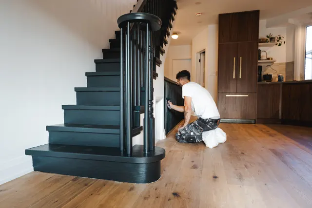 Mid-build: finishing carpentry on a new black-painted stair beside the walnut kitchen