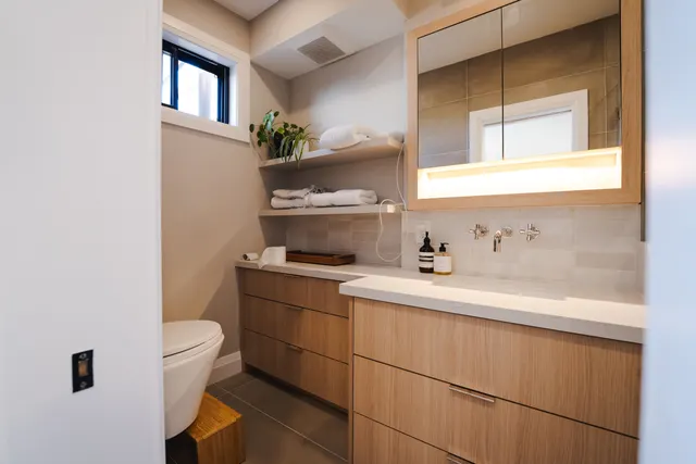 Bathroom with an oak vanity, a lit mirror cabinet and open shelving under a small window
