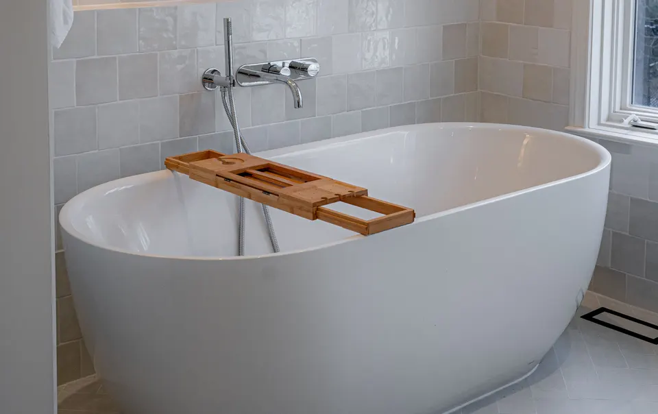 Bathroom with a freestanding tub, a bamboo bath caddy and a wall-mounted tub filler against handmade white tile