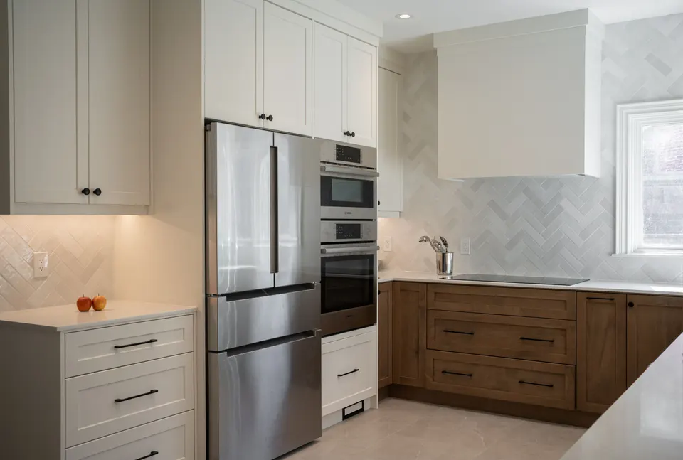 Kitchen with white upper cabinets and oak lowers, a stainless fridge and wall ovens, a white hood and a herringbone backsplash