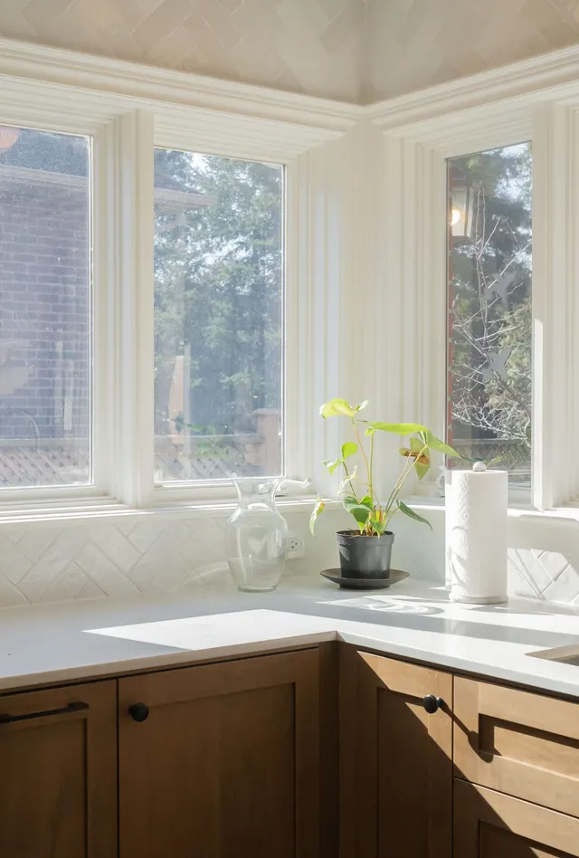 Corner sink under two windows, oak cabinets and a white herringbone backsplash with a potted plant
