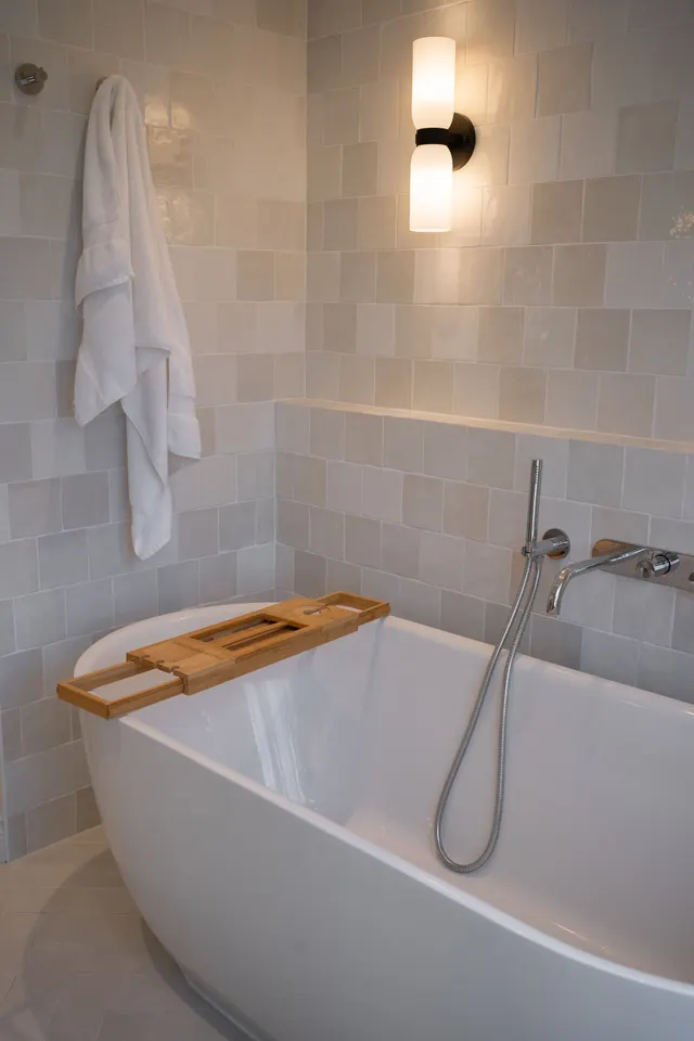 The freestanding tub under a black wall sconce, a white robe hanging on the tile