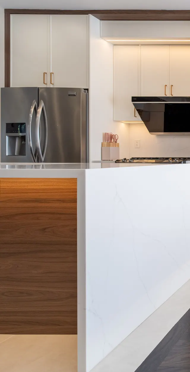 The end of the island: a white quartz waterfall over walnut panelling, with the stainless fridge and white cabinetry behind