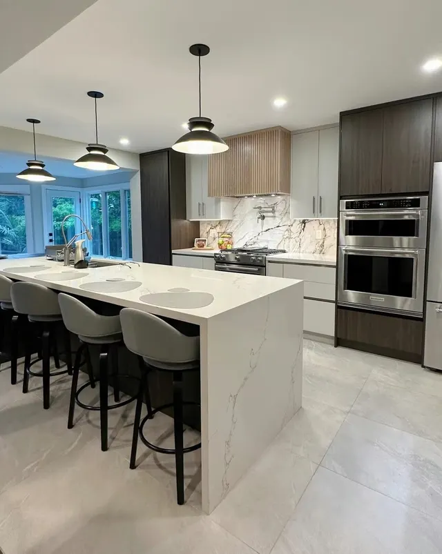 White quartz waterfall island with black stools under three black pendants