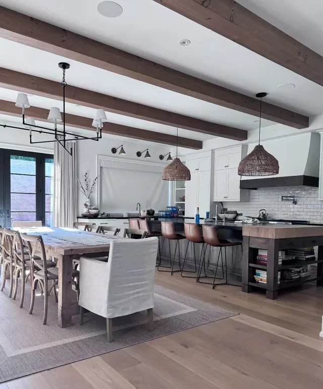 Beamed kitchen and dining room lit by woven pendants, a black chandelier and wall sconces
