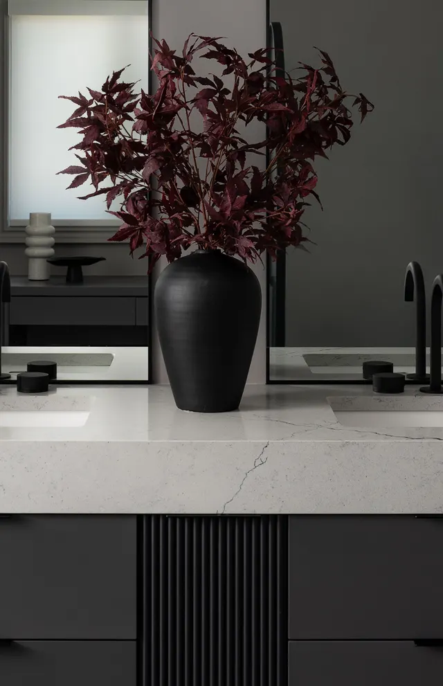 Black vase of red maple leaves on the white marble vanity top beside a black faucet