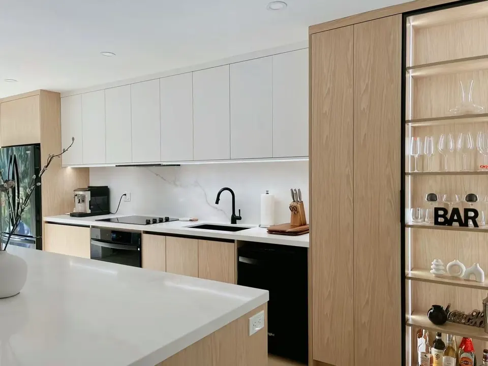 White and oak kitchen with a quartz island, a black faucet and a full-height oak wall