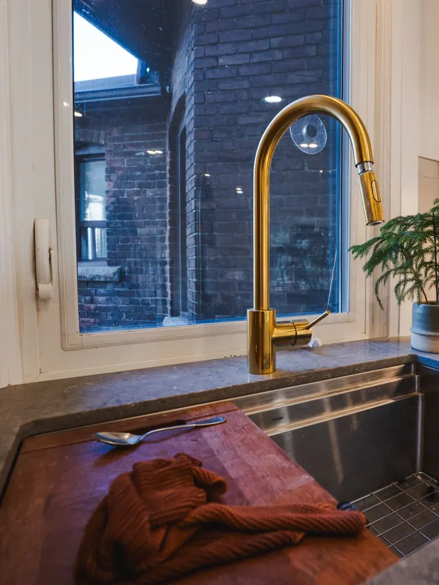 Brushed-gold faucet over a stone counter at the kitchen window