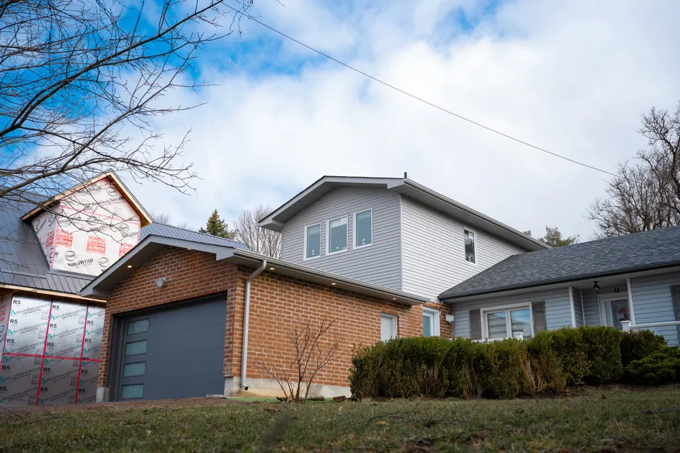 A three-storey addition clad in grey siding rising over the brick of the original house, with a new garage door below