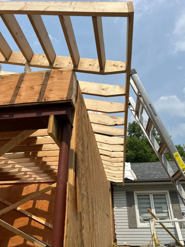 Looking up at new rafters and a steel post at the corner of the addition, a ladder against the framing