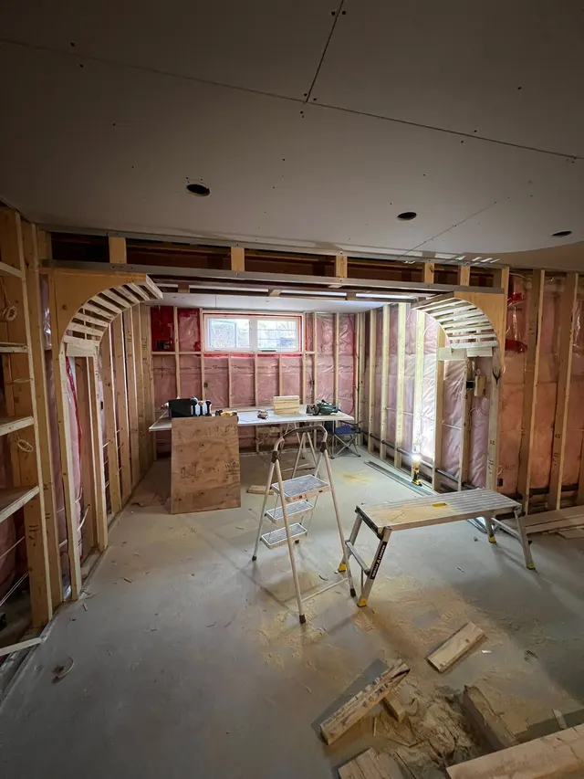 Basement mid-build: framed walls and arched openings with insulation behind, under a new drywall ceiling