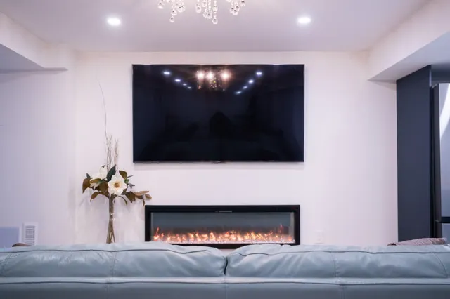 Basement living room with a linear electric fireplace under a wall-mounted TV, a crystal chandelier and a pale blue sofa