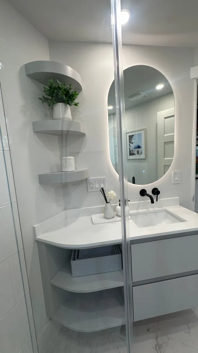 Floating grey vanity with a lit oval mirror, a black wall-mounted faucet and curved open shelves