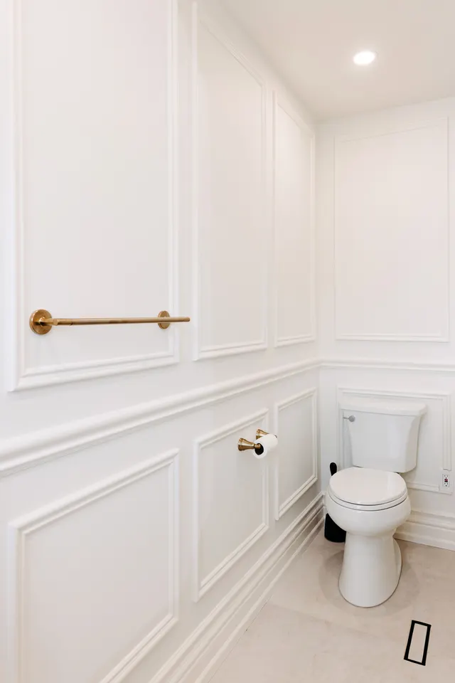 Wainscoted bathroom wall with a brushed-brass towel bar and paper holder beside the toilet