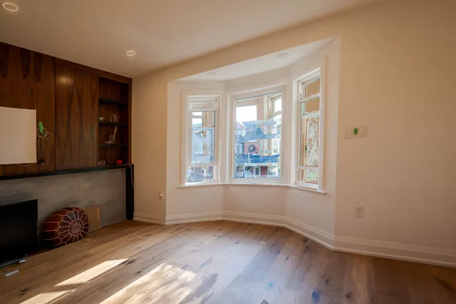 Living room with a sunlit bay window, wide-plank oak floors and a walnut built-in wall