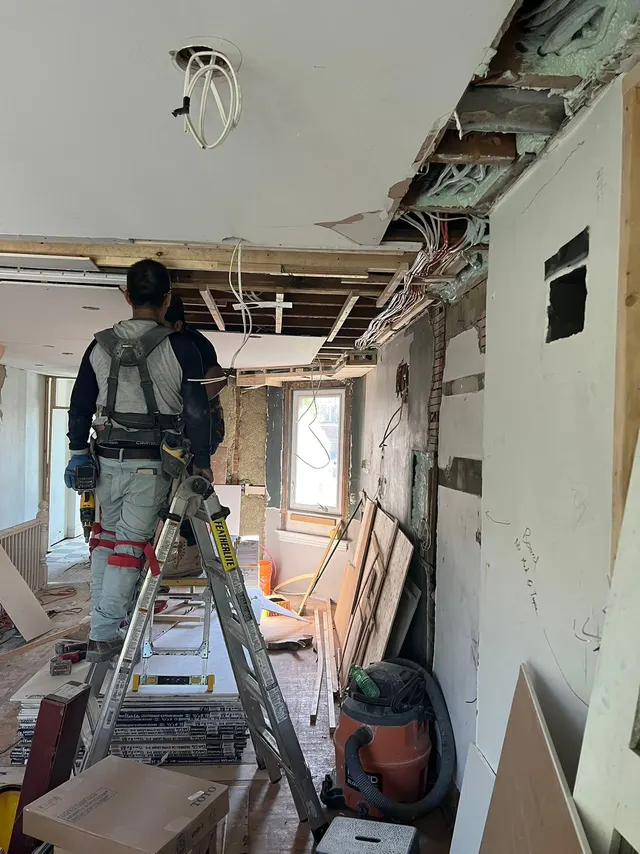 Mid-renovation: a worker on a ladder under an opened ceiling with the wiring exposed, in a gutted main floor