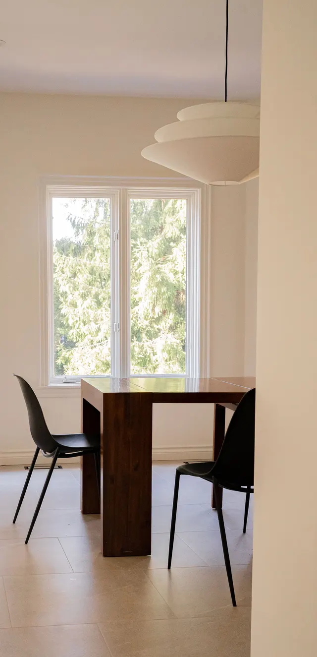 Dining corner with a walnut table and black chairs under a paper pendant, beside a tall window