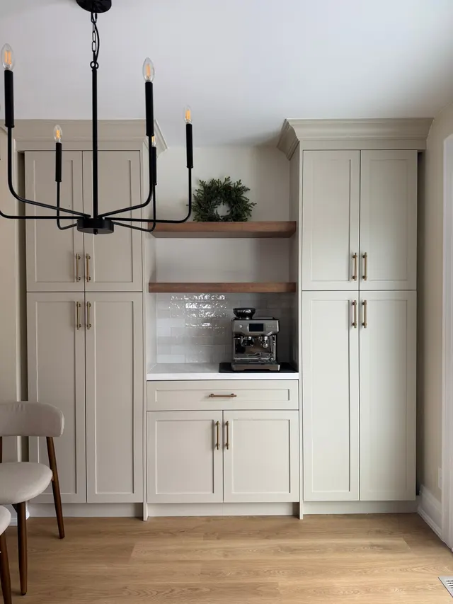 Built-in coffee station between tall shaker pantry cabinets, with walnut floating shelves and an espresso machine