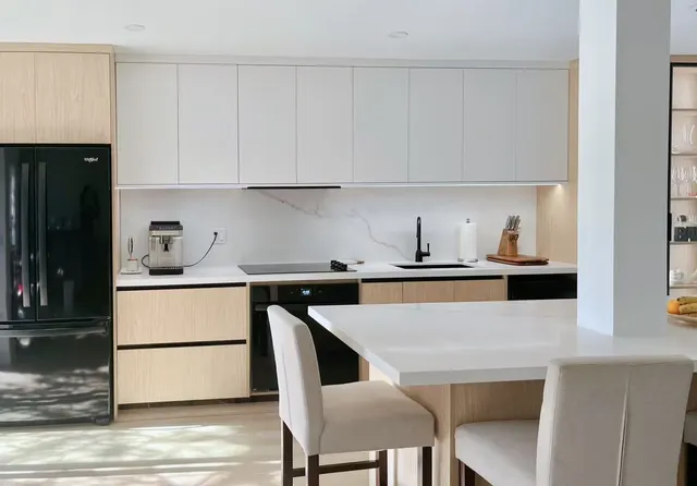 Kitchen with flat white uppers, pale oak lowers, a black fridge and a white quartz island with linen stools