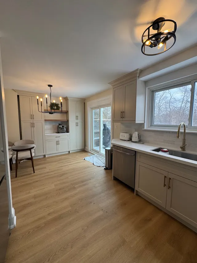 Greige shaker kitchen with a brass faucet under the window and a black iron chandelier over the dining corner